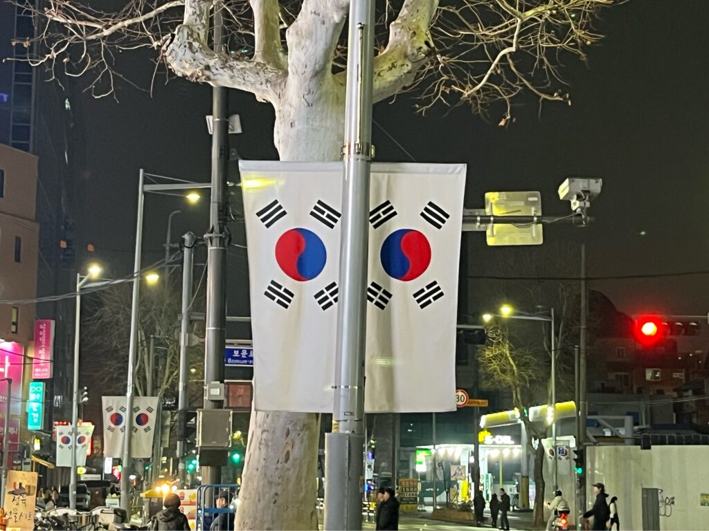 韓国旅行初心者ガイド!到着前にチェック!2026韓国旅行で知っておくべき基本情報 - photo 1773291786 大韓民国の国旗、太極旗(テグッキ)です。白地は明るさと純粋さ、平和を愛する民族性を表し、中央の太極模様は陰と陽の調和を象徴しています。